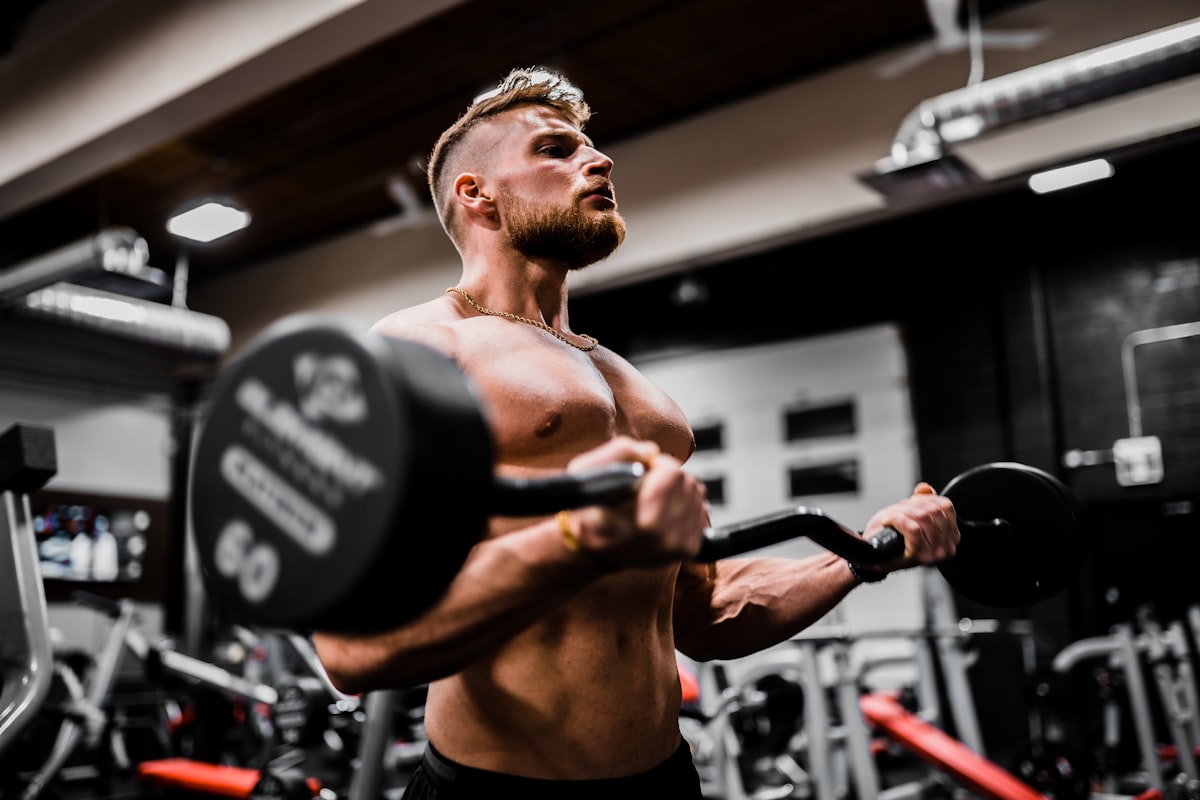 Persona entrenando con barra Z en un gimnasio de luz tenue, gesto de esfuerzo